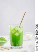 Cold refreshing healthy matcha made of green tea leaves ground powder served with ice and drinking paper straw on white wooden kitchen table with ingredients as organic antioxidant vitamin drink. Стоковое фото, фотограф Елена Кабенкина / Фотобанк Лори