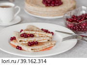 Russian traditions. Russian holiday Maslenitsa. Still life with a cup of tea, a stack of pancakes with northern cranberries, cubes of butter on the table. Стоковое фото, фотограф Photojuli / Фотобанк Лори