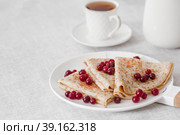 Russian traditions. Russian holiday Maslenitsa. Still life with a cup of tea, a stack of pancakes with northern cranberries, cubes of butter on the table. Стоковое фото, фотограф Photojuli / Фотобанк Лори