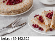 Russian traditions. Russian holiday Maslenitsa. Still life with a cup of tea, a stack of pancakes with northern cranberries, cubes of butter on the table. Стоковое фото, фотограф Photojuli / Фотобанк Лори