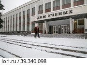 Город Обнинск, проспект Ленина, 129. Мужчина и женщина проходят мимо входа в Дом ученых (МП "Дом ученых") в зимний пасмурный день (2021 год). Редакционное фото, фотограф Наталья Николаева / Фотобанк Лори