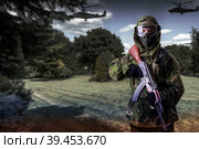 A soldier in camouflage uniform with a rifle in his hands against the background of the forest with helicopters, looks into the camera. The concept of guerrilla warfare or the game of airsoft. Стоковое фото, фотограф Владимир Арсентьев / Фотобанк Лори