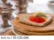 Русские традиции. Русский праздник Масленица. Натюрморт с чашкой чая, стопкой блинов, красной икрой, лимоном, рогаликами, леденцовым петушком, деревянными ложками (хохлома) и самоварами. Стоковое фото, фотограф Photojuli / Фотобанк Лори