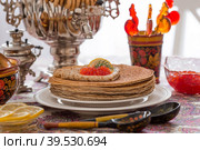Русские традиции. Русский праздник Масленица. Натюрморт с чашкой чая, стопкой блинов, красной икрой, лимоном, рогаликами, леденцовым петушком, деревянными ложками (хохлома) и самоварами. Стоковое фото, фотограф Photojuli / Фотобанк Лори
