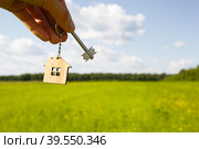 Wooden pendant of a house and key. Background of the sky and field. Dream of home, building a cottage in the countryside, plan and design, delivery of the project, moving to a new house. Copy space. Стоковое фото, фотограф Ольга Симонова / Фотобанк Лори