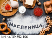 Русские традиции. Русский праздник Масленица. Стопка блинчиков, красная икра, бублики, рогалики, деревянная ложка, яйца и сливочное масло. Надпись на русском языке "Масленица" написано мукой. Вид сверху. Стоковое фото, фотограф Photojuli / Фотобанк Лори