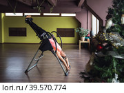 Woman doing therapy, resting after workout, hanging upside down on inversion table. Стоковое фото, фотограф Сергей Чайко / Фотобанк Лори