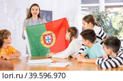 Female teacher, conducting extracurricular lesson in the school class tells schoolchildren the history of Portugal and shows national flag of country. Стоковое фото, фотограф Яков Филимонов / Фотобанк Лори
