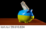 Купюра номиналом "1" доллар торчит из копилки, которая раскрашена в цвета украинского флага. Редакционное фото, фотограф Семён Прудий / Фотобанк Лори