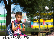 Little girl with a backpack and in a school uniform in the school yard plays pop it toy. Back to school, September 1. The pupil relaxes after lessons. Primary education, elementary class for student. Стоковое фото, фотограф Ольга Симонова / Фотобанк Лори