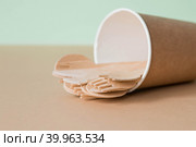 Экологически чистая одноразовая кухонная утварь в бумажном стаканчике на бежево-зеленом фоне. Деревянные вилки, ложки и ножи. Экология, концепция нулевых отходов. Стоковое фото, фотограф Photojuli / Фотобанк Лори