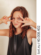 Teen girl model in black clothes grimacing showing sign peace at grey background, looking at camera. Teenage girl shooting posing in studio. Fashion style concept. Copy text space for advertising. Стоковое фото, фотограф Aleksandr Golubev / Фотобанк Лори
