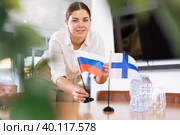 Positive young woman putting flag of Russia on the table with flag of Finland in conference room. Стоковое фото, фотограф Яков Филимонов / Фотобанк Лори