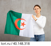 Confident middle-aged woman waving national flag of Algeria while looking at camera at gray wall background. Стоковое фото, фотограф Яков Филимонов / Фотобанк Лори