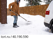 A man in winter cleans snow with a shovel in the yard of a house in the parking lot. Snowfall, difficult weather conditions, the car is stalling, digging up the passage. Стоковое фото, фотограф Ольга Симонова / Фотобанк Лори