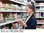A young smiling woman chooses and buys yogurts in a store. Стоковое фото, фотограф Владимир Разгуляев / Фотобанк Лори