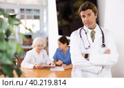 positive medical male colleague standing in meeting room and employees are talking behind him at table. Стоковое фото, фотограф Яков Филимонов / Фотобанк Лори