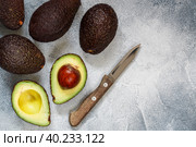 Whole and cut in half ripe organic avocados and a knife on a grey  background. The Haas Avocado. Source of vitamins , trace elements , beta-carotene and omega-3 fatty acids . Healthy food, diet. Стоковое фото, фотограф Виктория Панченко / Фотобанк Лори