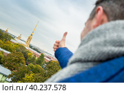 Мужчина показывает жест рукой — это хорошо, это круто, большой палец вверх. На фоне исторических достопримечательностей города Санкт-Петербург, Россия. Петропавловская крепость и собор. Стоковое фото, фотограф Андрей Степанов / Фотобанк Лори