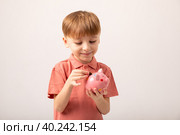Cute smiling little boy putting coin into pink piggy bank. Adorable preschool child kid saving money for future, insurance and investment concept. The child manages and deposits his finances. Стоковое фото, фотограф Ирина Михайличенко / Фотобанк Лори