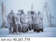 Памятник революционерам на берегу Анадырского лимана. Вид на покрытые инеем и снегом скульптуры и краны морского порта. Мемориальный комплекс первому ревкому Чукотки. Город Анадырь, Чукотка, Россия. Редакционное фото, фотограф Андрей Степанов / Фотобанк Лори