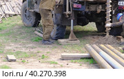 Team of workers with drilling rig on car are drilling artesian well for water in ground. Insertion of metal casing pipe into ground, installation of individual drinking supply, June 28, 2022, Russia, Palaces. Редакционное видео, видеограф Ольга Симонова / Фотобанк Лори