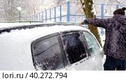 A man brushes snow from a car after a snowfall. A hand in jacket with a car broom on the white body. Winter weather conditions. Slow Motion. Стоковое видео, видеограф Ольга Симонова / Фотобанк Лори