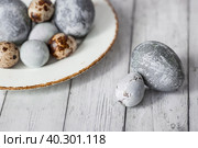 Stylish grey Easter eggs in the color of marble, concrete in a plate and willow branches on a white wooden background. Coloring eggs with natural dye karkade tea. Environmental friendliness. Naturalness. The feast of bright Easter. Стоковое фото, фотограф Photojuli / Фотобанк Лори