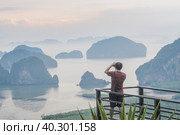 A photographer photographs a beautiful view from the Samet Nanghse observation deck in Thailand.Morning view of the blue mountains and stones in the water in Thailand, mysterious beauty. Tourism travel and landscape photography. Стоковое фото, фотограф Владимир Разгуляев / Фотобанк Лори