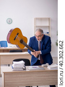 Old male employee playing guitar at workplace. Стоковое фото, фотограф Elnur / Фотобанк Лори