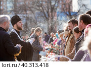 Russia, the City of Vidnoye, April 15, 2023. Easter service. The priest sprinkles people and Easter treats with holy water at the entrance to the temple. People go to sanctify eggs and cakes. Редакционное фото, фотограф Photojuli / Фотобанк Лори