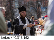 Russia, the City of Vidnoye, April 15, 2023. Easter service. The priest sprinkles people and Easter treats with holy water at the entrance to the temple. People go to sanctify eggs and cakes. Редакционное фото, фотограф Photojuli / Фотобанк Лори