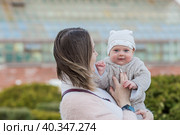 A young mother holds a charming little son in her arms. The kid looks at the camera and smiles. Portrait of a beautiful chubby 4-month-old baby. Стоковое фото, фотограф Photojuli / Фотобанк Лори