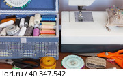 Seamstress workplace at home. Sewing machine, blue box with sewing supplies, accessories: skeins of colorful threads, pins, needles, measuring tape on wooden table. Needlework, craft, DIY concept. Стоковое видео, видеограф Виктория Катьянова / Фотобанк Лори