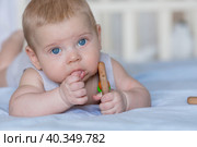 A charming boy in a bright bedroom. A newborn baby is lying on the bed and gnawing on toys. Teeth are teething. The baby's gums are itching. Family, pregnancy and childbirth. Стоковое фото, фотограф Photojuli / Фотобанк Лори