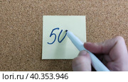 Надпись 50% на бумажном стикере приклеенном к пробковой  доске. Женщина пишет маркером на желтой бумаге. Синий фломастер в женской руке. Рукописный текст красивым почерком. Процент скидки или прибыли. The inscription is 50% on a paper sticker glued to a cork board. A woman writes with a marker on yellow paper. A blue felt-tip pen in a woman's hand. Handwritten text in a beautiful handwriting. Percentage of discount or profit. Стоковое видео, видеограф Ирина / Фотобанк Лори