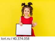 little brunette girl in red drees smiling and holding an empty drawing Board, space for text,isolate on a yellow background. Стоковое фото, фотограф Ирина Михайличенко / Фотобанк Лори