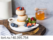 Cottage cheese pancakes, Russian cheesecakes with fresh blueberries, strawberries, honey and mint leaves on a stylish wooden board on a gray concrete table. Natural products. Healthy and delicious breakfast. Стоковое фото, фотограф Photojuli / Фотобанк Лори