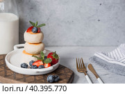 Cottage cheese pancakes, Russian cheesecakes with fresh blueberries, strawberries and mint on a stylish wooden board on a gray concrete table. Natural products. Healthy and delicious breakfast. Стоковое фото, фотограф Photojuli / Фотобанк Лори