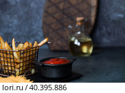 French fries in a metal basket with salt, ketchup and sunflower oil on a stylish board on a dark background. Fried potatoes. The concept of fast food and junk food. Стоковое фото, фотограф Photojuli / Фотобанк Лори