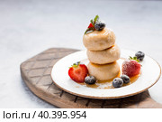 Cottage cheese pancakes, Russian cheesecakes with fresh blueberries, strawberries, honey and mint leaves on a stylish wooden board on a gray concrete table. Natural products. Healthy and delicious breakfast. Стоковое фото, фотограф Photojuli / Фотобанк Лори
