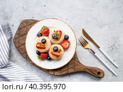 Cottage cheese pancakes, Russian cheesecakes with fresh blueberries, strawberries, honey and mint leaves on a stylish wooden board on a gray concrete table. Natural products. Healthy and delicious breakfast. Стоковое фото, фотограф Photojuli / Фотобанк Лори