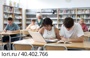 Asian schoolgirl, studying with a classmate guy in the school library on a laptop and making notes in a copybook, preparing for lessons. Стоковое видео, видеограф Яков Филимонов / Фотобанк Лори