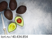 Whole and cut in half ripe organic avocados and a knife on a grey background. The Haas Avocado. Source of vitamins , trace elements , beta-carotene and omega-3 fatty acids . Healthy food, diet. Стоковое фото, фотограф Виктория Панченко / Фотобанк Лори