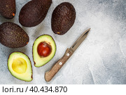 Whole and cut in half ripe organic avocados and a knife on a grey background. The Haas Avocado. Source of vitamins , trace elements , beta-carotene and omega-3 fatty acids . Healthy food, diet. Стоковое фото, фотограф Виктория Панченко / Фотобанк Лори