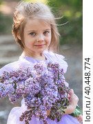 Spring flowering. Portrait of a beautiful little girl 4 years old in a lilac dress with a bouquet of lilac flowers in nature. Childhood. The baby poses and looks at the camera. Стоковое фото, фотограф Photojuli / Фотобанк Лори