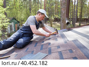 A man mounts soft bitumen shingles with nails and a hammer on the roof of a country house. Стоковое фото, фотограф Кутина Татьяна / Фотобанк Лори