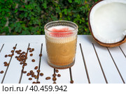 Raf coffee coconut with fresh coconut and coffee beans on white wooden table against green leaves with copy space. Стоковое фото, фотограф Татьяна Терехина / Фотобанк Лори