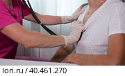 A girl doctor in a mask listens with a stethoscope to the chest of an adult woman. A woman in the doctor's office complains of a cough. Стоковое видео, видеограф Юрий Поздников / Фотобанк Лори