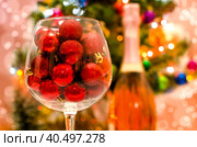 Red glitter balls in a large wine glass close up against the background of a decorated Christmas tree. Стоковое фото, фотограф Артем Курутин / Фотобанк Лори